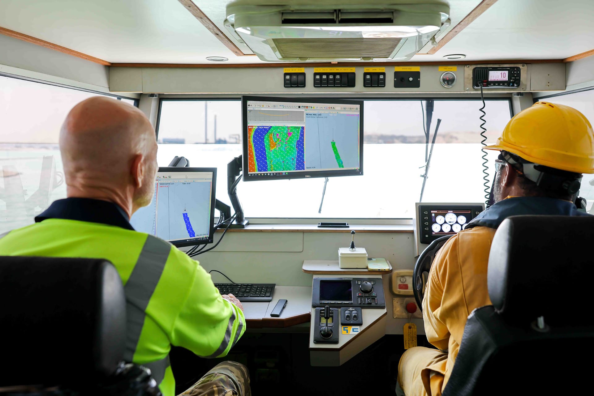Wide view of a survey wheelhouse with a surveyor and helmsman working at multibeam display screens.