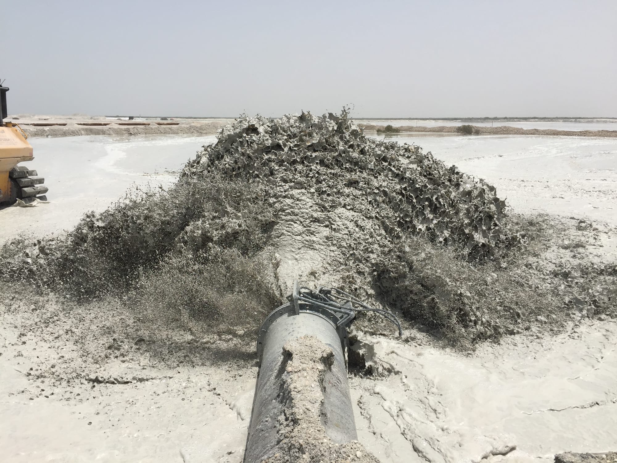 Discharge pipeline outfall pumping sand slurry onto a reclamation area at dusk.