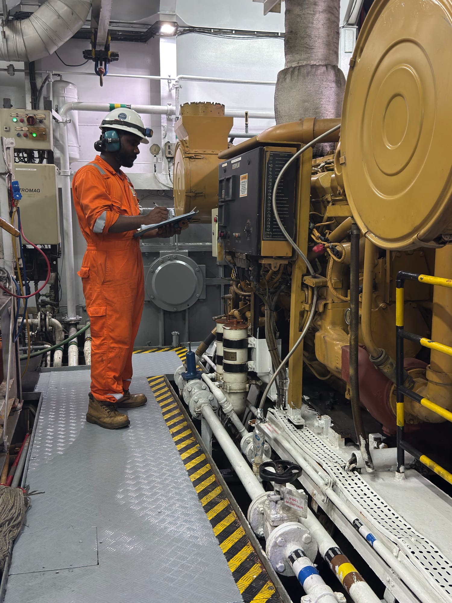 Gulf Cobla engineer in coveralls taking readings beside a main engine in the engine room.